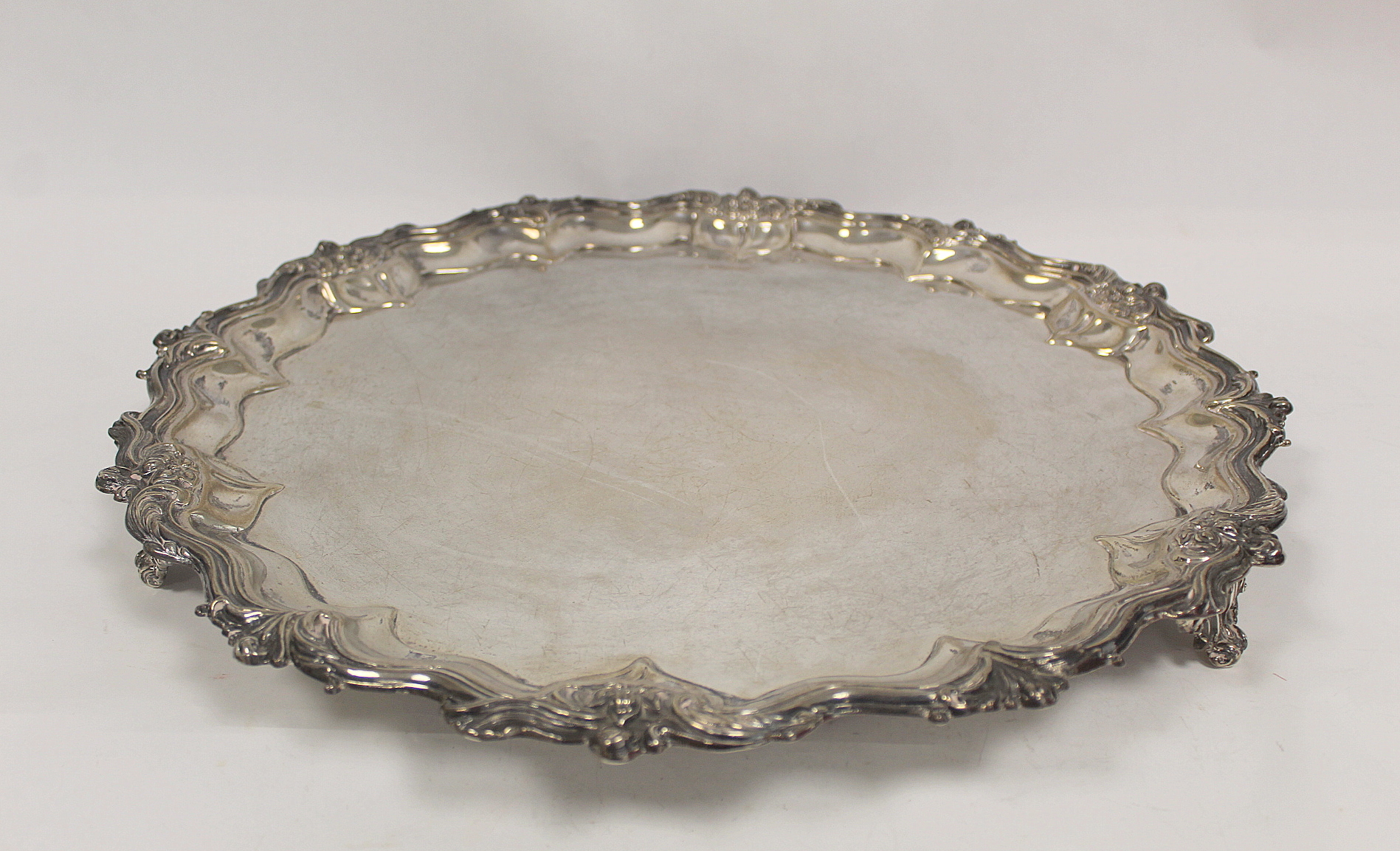 Silver circular tray with shaped moulded floral and leafage border on similar feet, by Walker &