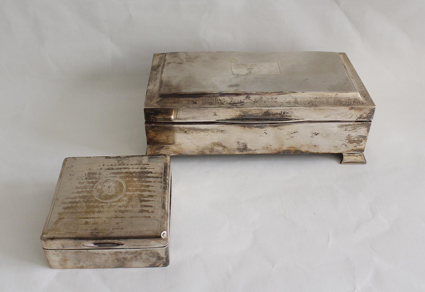 Silver engine turned cigarette box on bracket feet, 19cm and another smaller. (2)