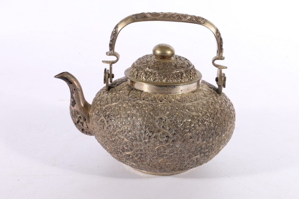 Indian white metal relief decorated tea pot with swing handle, stamped "900" to the base, 486g gross