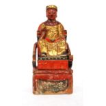 Chinese red and gilt carved wood figure of a dignitary upon a throne, in two parts, 25.5cm high.