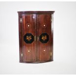 A George III mahogany bowfront hanging corner cupboard, the two doors inlaid with floral sprays