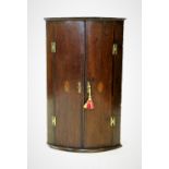 A George III oak bow front hanging corner cupboard, the pair of convex doors centred with an