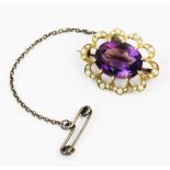 An Edwardian amethyst and seed pearl cluster brooch, the central oval faceted amethyst measuring