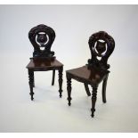 A pair of Victorian mahogany hall chairs, with a carved scrolling openwork back, centred with a