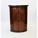 A George III mahogany bow front hanging corner cupboard, the cross banded doors applied with 'H'