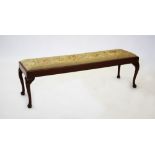 A 20th century mahogany long foot stool, the rectangular needlework upholstered seat raised upon