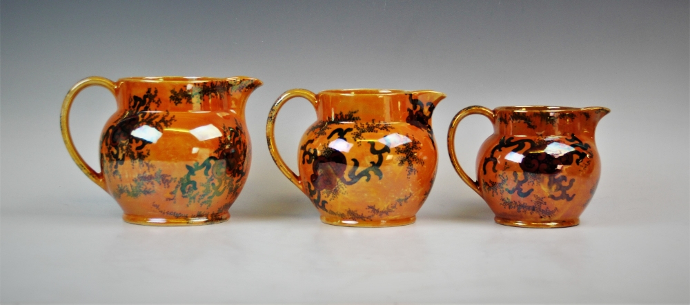 Three graduated Bursley ware Dragon pattern lustre jugs by Frederick Rhead, applied with fiery