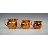 Three graduated Bursley ware Dragon pattern lustre jugs by Frederick Rhead, applied with fiery