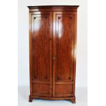 An Edwardian mahogany bow front wardrobe, with a moulded cornice above a pair of doors applied