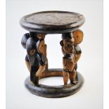 A Nigerian Yoruba tribal stool, of circular form, designed with four figural legs, alternating Ibeji