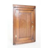 A George III oak flat front hanging corner cupboard, the single panelled door mounted on 'H' brass