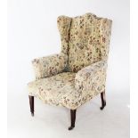 An Edwardian wing back armchair, the arched padded back with out swept wing back and arms, over a
