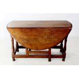 An early 19th century oak drop leaf dining table, the oval top with a carved border, raised upon