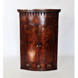 A George III mahogany bow front hanging corner cupboard, the frieze applied with turned beading