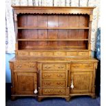 A late George III honey oak dresser, the moulded cornice above a wavy frieze and two shelves,