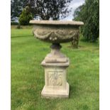 A cast concrete bowl shaped urn on stand, the urn cast in relief with garland and pendulum drops