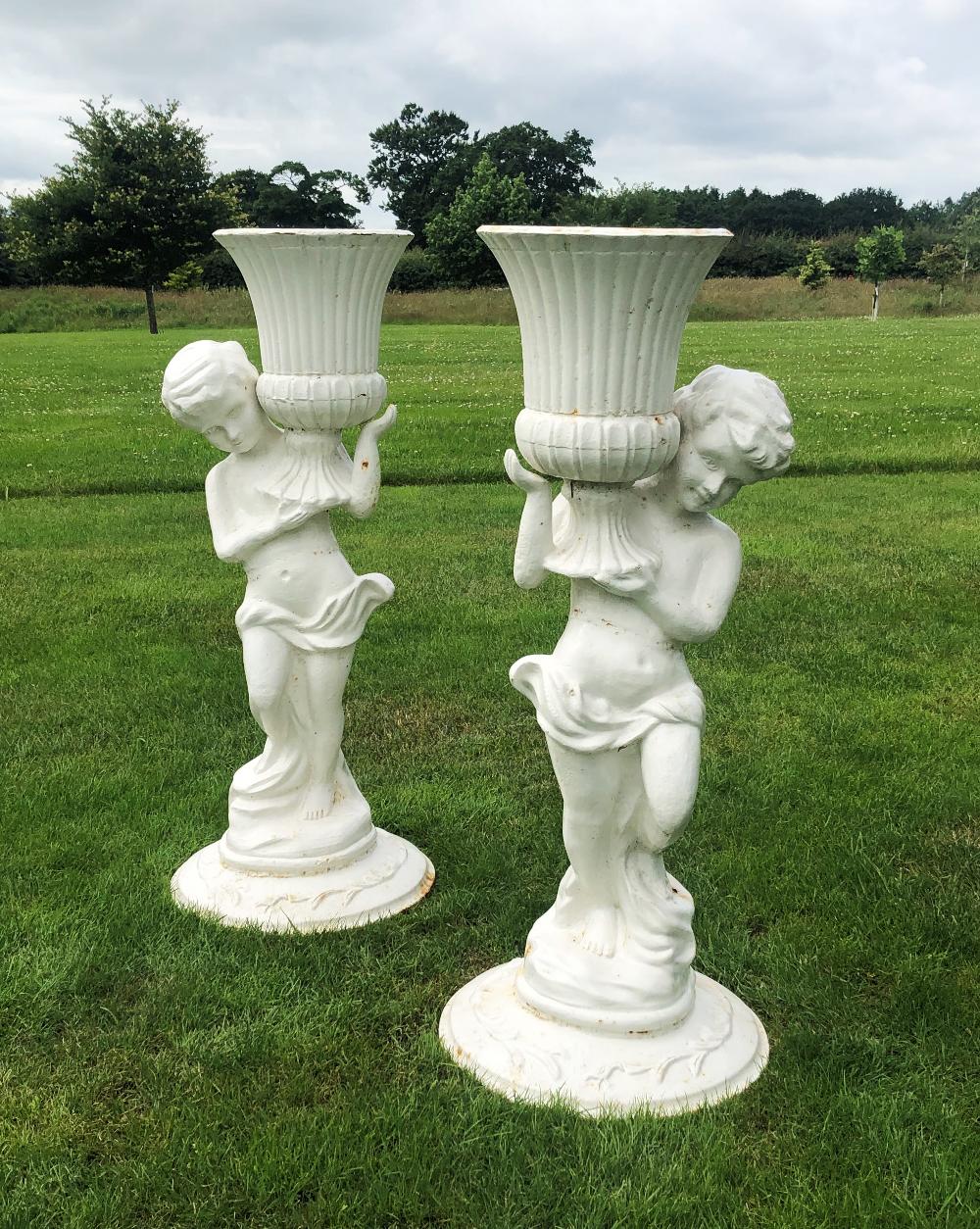 A pair of cast iron figural jardinieres, white painted, each modelled as a scantily clad putti