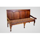 A George III oak settle, with four fielded panels above a later upholstered seat, enclosed by down
