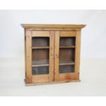 A Victorian pine glazed wall cabinet, with a moulded cornice above two glazed doors enclosing