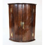 A George III oak bow front hanging corner cupboard, the pair of doors on 'H' brass hinges, enclosing