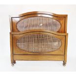 An early 20th century mahogany and rattan bedstead, the arched head and foot board inset with an