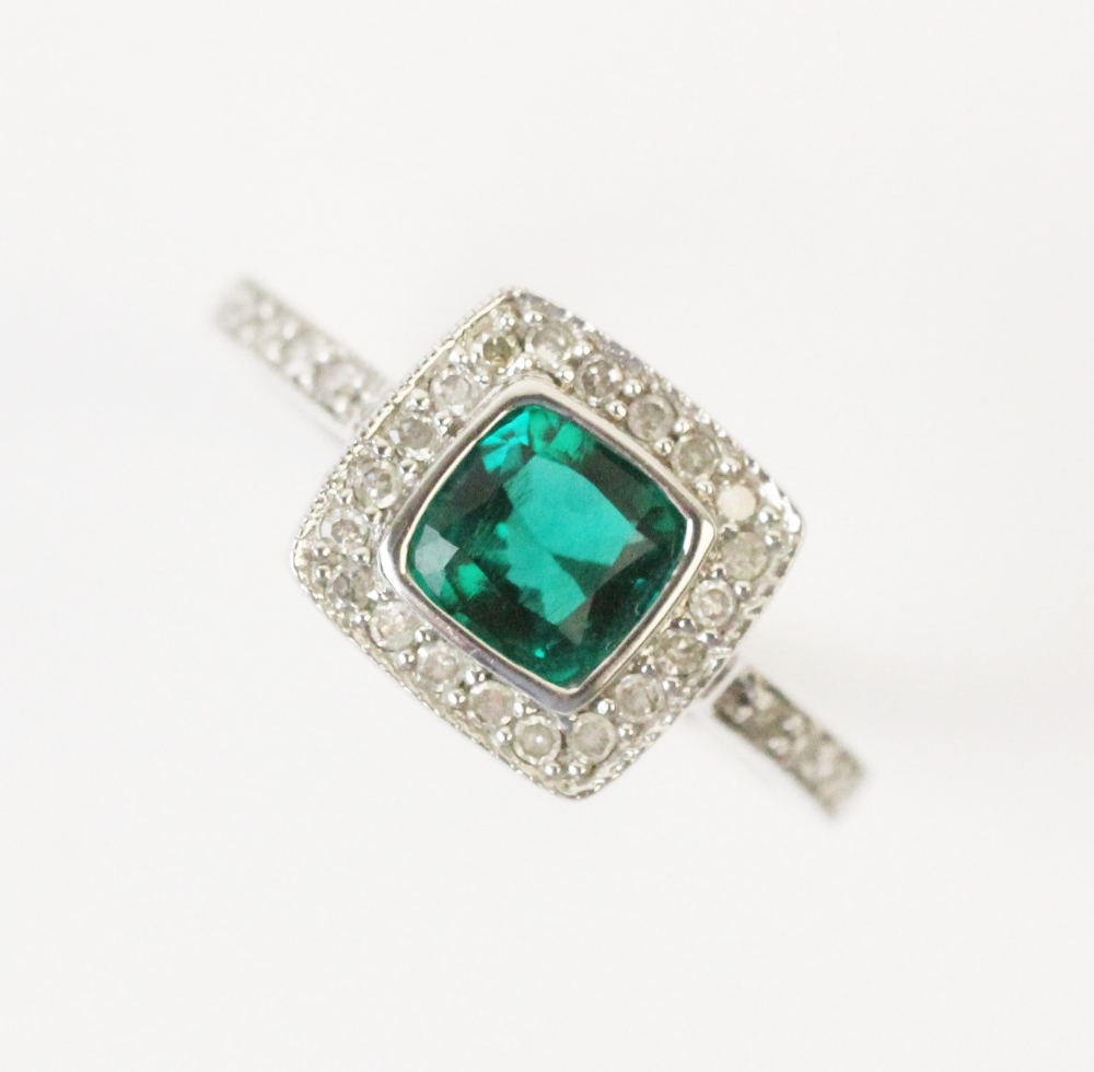 A synthetic emerald and diamond ring, comprising a central cushion cut synthetic emerald measuring