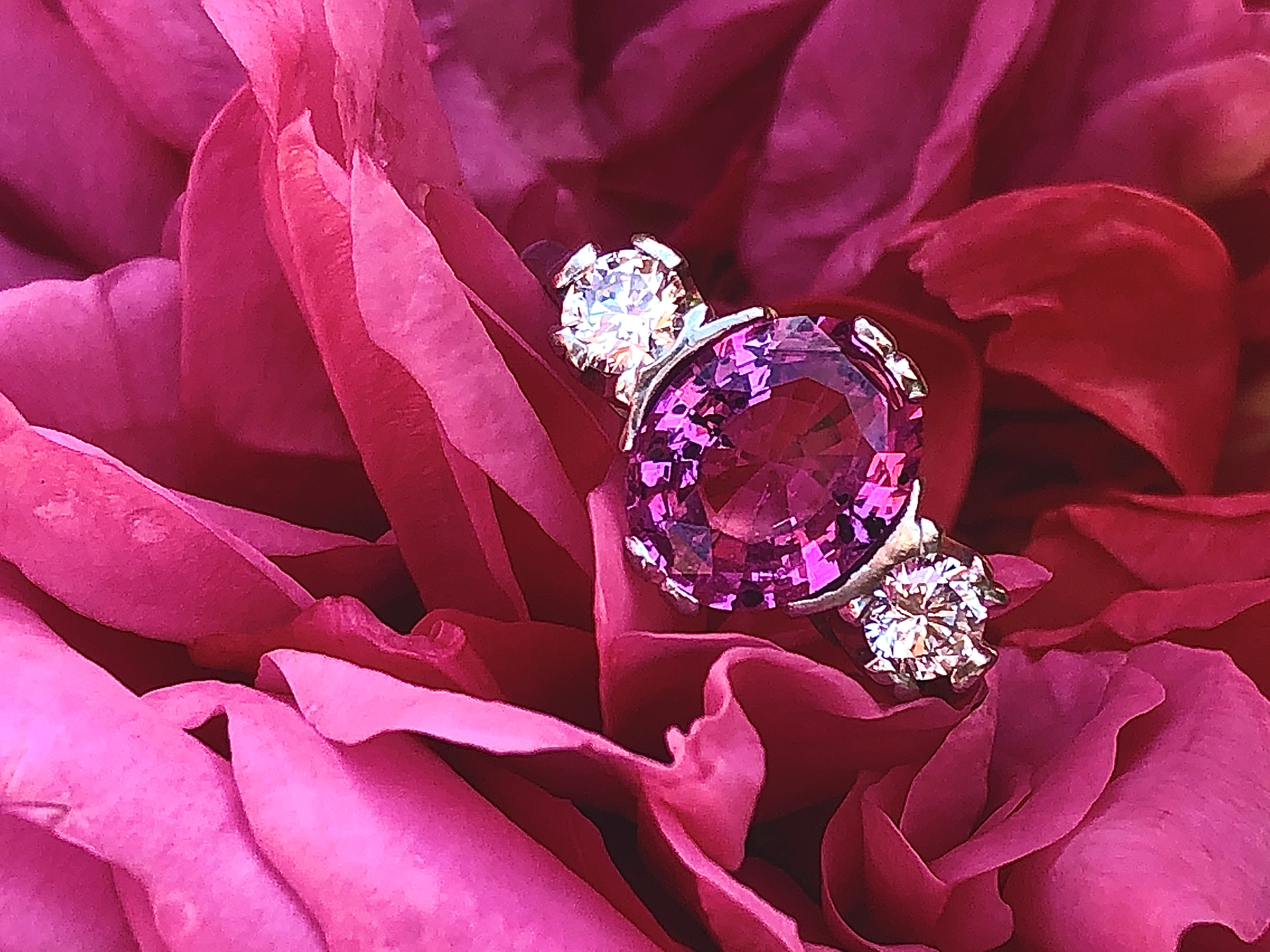 A pink sapphire and diamond ring, the central oval cut untreated vivid pink sapphire measuring