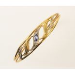 A 9ct gold sapphire and diamond set bangle, the central pierced scrolling panel set with an oval