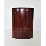A George III bow front mahogany hanging corner cupboard, the upper frieze inlaid with two