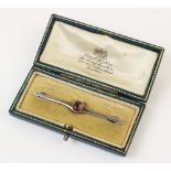 An early 20th century bar brooch, comprising a central oval mixed cut red gemstone, measuring 6mm
