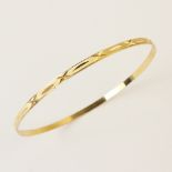 An 18ct yellow gold bangle, the round bangle with engine turned decoration to exterior, lozenge