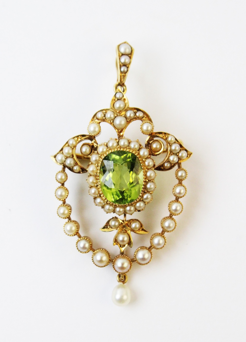 An Edwardian style peridot and seed pearl pendant/brooch, the central oval mixed cut peridot