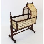 A Victorian mahogany and rattan cradle, with turned finials upon an onion shaped rattan canopy and