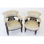 A pair of Victorian walnut and upholstered tub chairs, each with a padded back and arm rest, upon