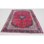 A large Persian mashad carpet, with traditional floral medallion design against a puce ground, 375cm