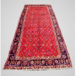 A large red ground Persian Tabriz runner, with all over design and vibrant blue border, 381cm x