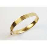 A 9ct gold hinged bangle, of oval form with engine turned decoration to exterior, with tongue and