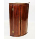 A George III mahogany bow front hanging corner cupboard, the pair of convex doors inlaid with