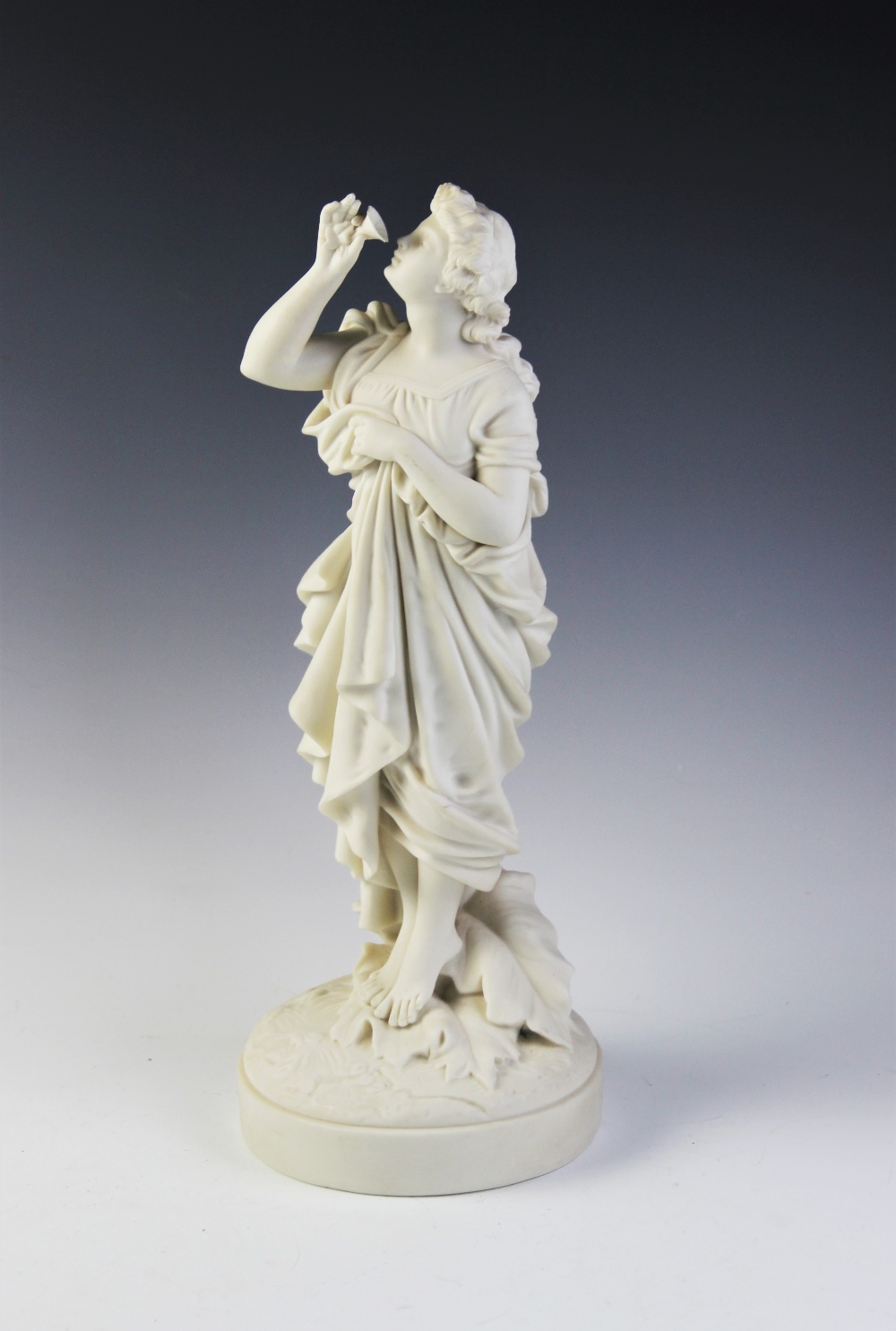 A Parian ware figure of a flower picker, modelled standing with her hand aloft smelling a flower,