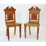 A pair of Victorian golden oak hall chairs, each with a broken swan neck pediment above a panel