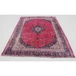 A large Persian Mashad carpet, with traditional floral medallion design against a puce ground, 375cm