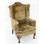 A George I style wing back fireside armchair, early 20th century, covered in embossed foliate