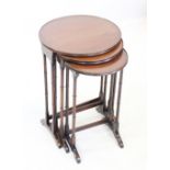 An Edwardian mahogany nest of tea tables, each with a circular tray top raised upon slender ring