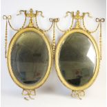 A pair of 19th century gilt wood and gesso oval wall mirrors, each with an Adams style, urn shaped