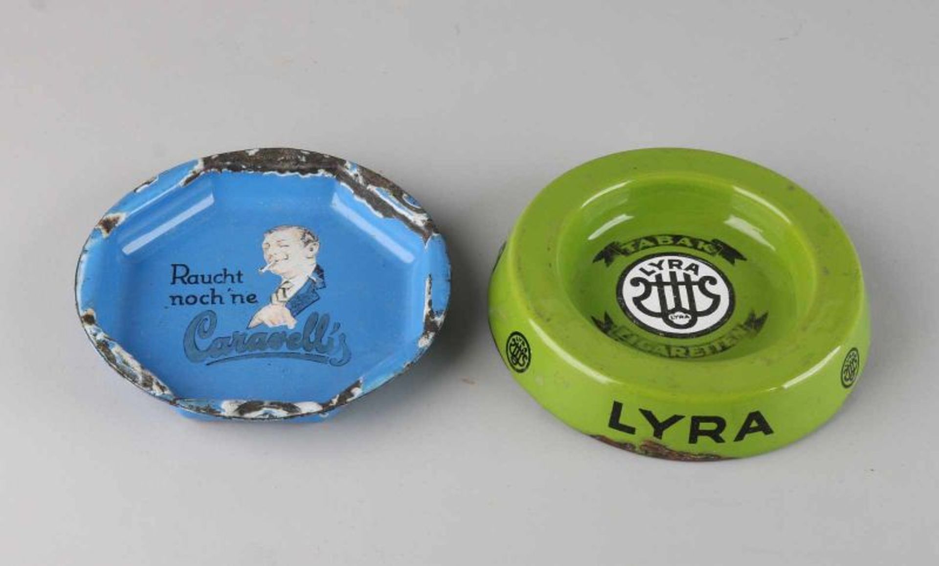 Two enamelled ashtrays with advertising. 20th century. Comprising: Rauch noch'ne Caravellis and Lyra