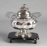 Silbernes Tabakglas mit Deckel, 833/000, auf einen schwarzen Holzsockel mit Kugelfüßen gestellt.