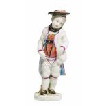 SMALL PORCELAIN FIGURE OF A BOY IN TRADITIONAL DRESS WITH SHOULDER BAG.