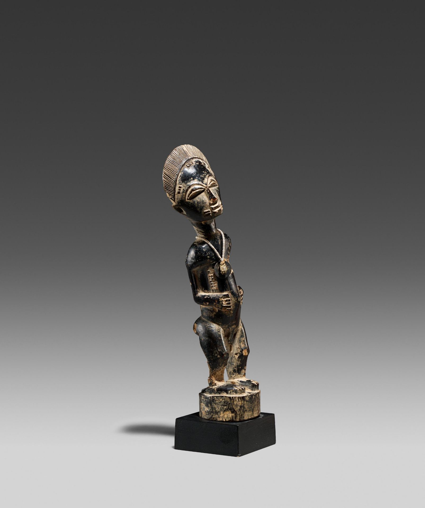 BAULE, Ivory Coast. Male figure. Wood, pearl necklace with a French coin (50 centimes), dark patina.