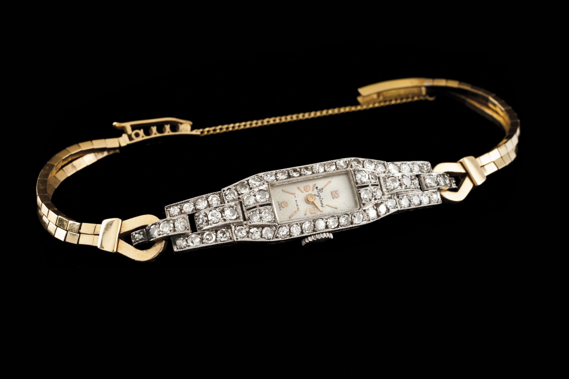 A Regines Art Deco watchPlatinum and goldChiselled rectangular case with loops set with 62 8/8 cut