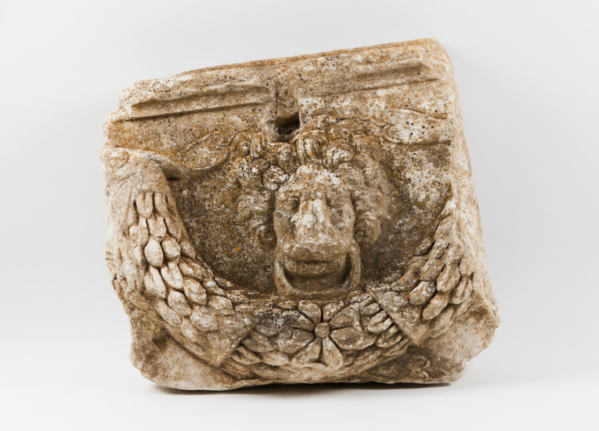 A carved stone fragmentMarbleLow-relief decoration of lion's head with ring and laurel wreath60x66